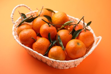 Photo of Fresh ripe tangerines and leaves in basket on orange table
