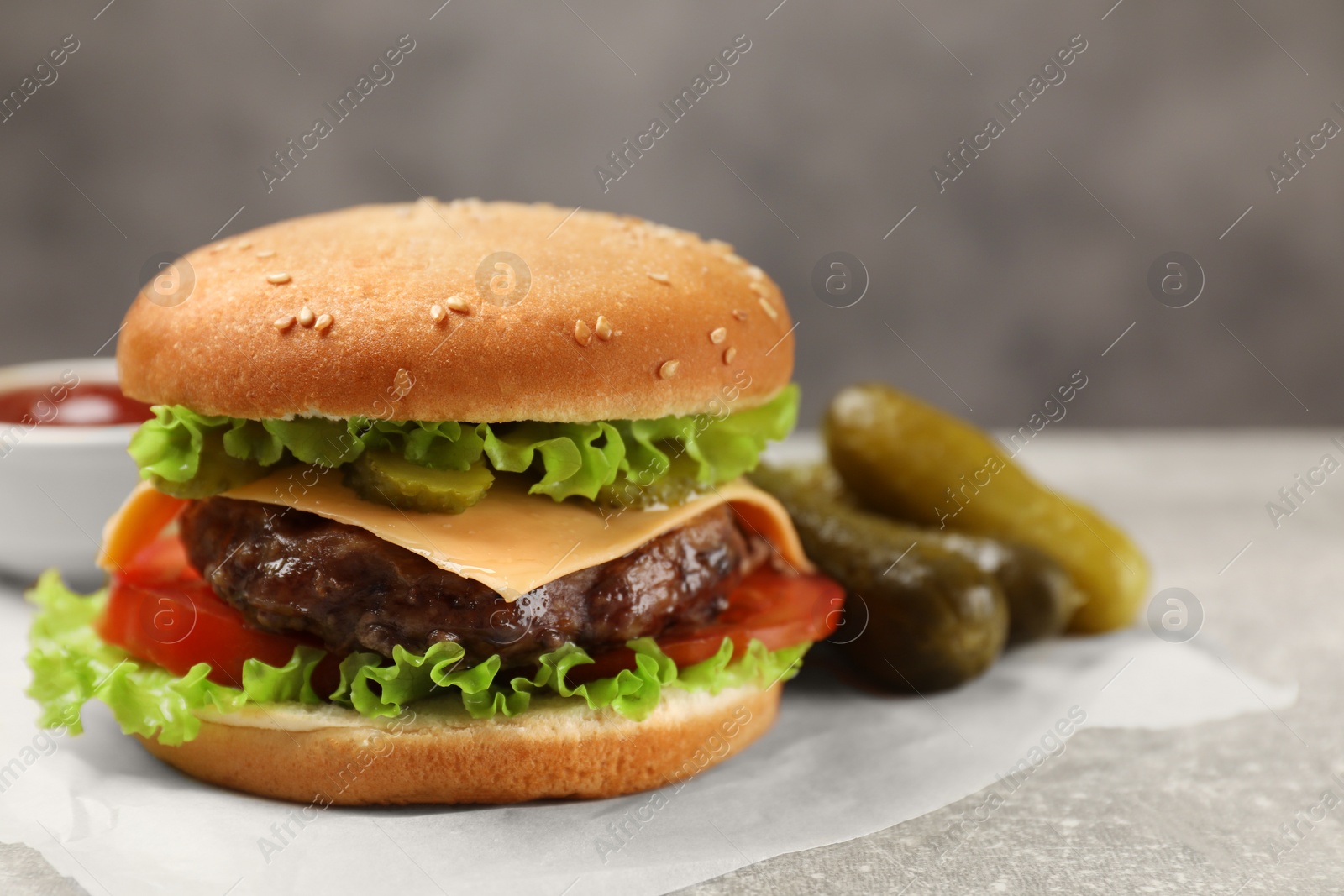 Photo of Tasty hamburger with patty and pickles on light grey table, closeup. Space for text