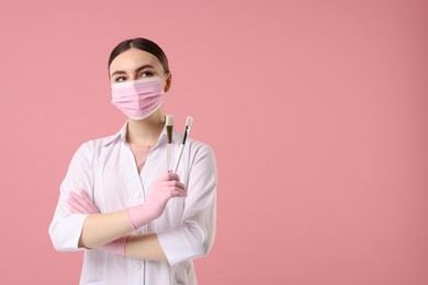 Photo of Cosmetologist with cosmetic brushes on pink background, space for text