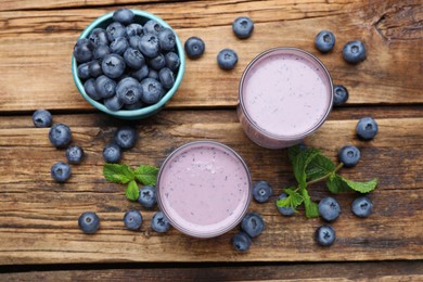 Glasses of blueberry smoothie with mint and fresh berries on wooden table, flat lay