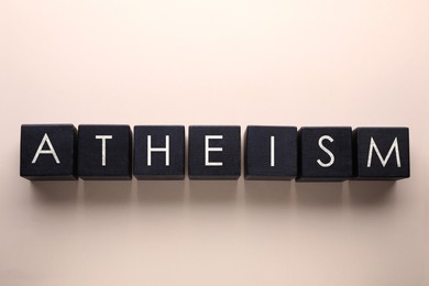 Image of Word Atheism made of black wooden squares with letters on beige background, top view