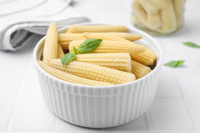 Canned baby corns with basil on white tiled table, closeup