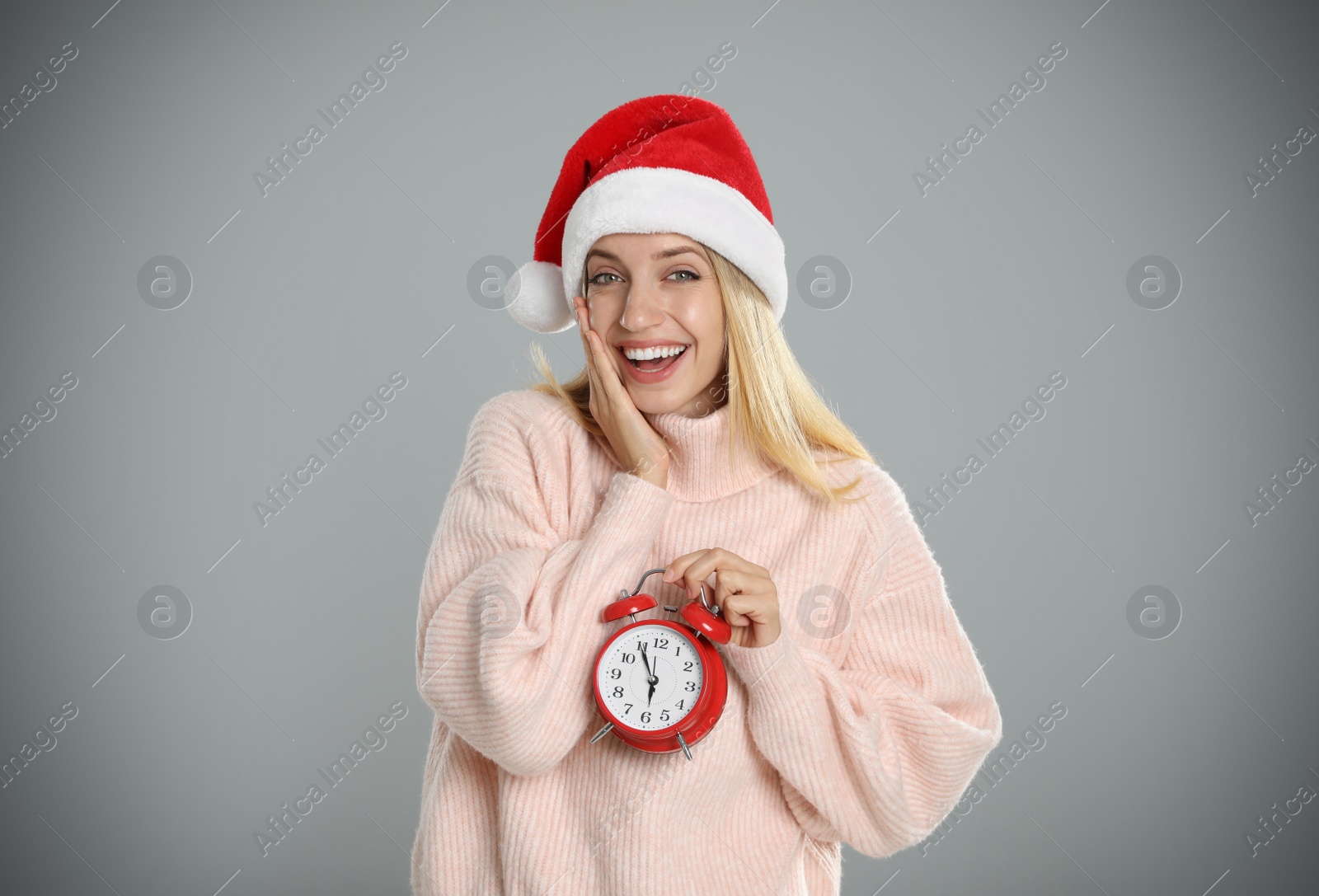 Photo of Woman in Santa hat with alarm clock on grey background. New Year countdown