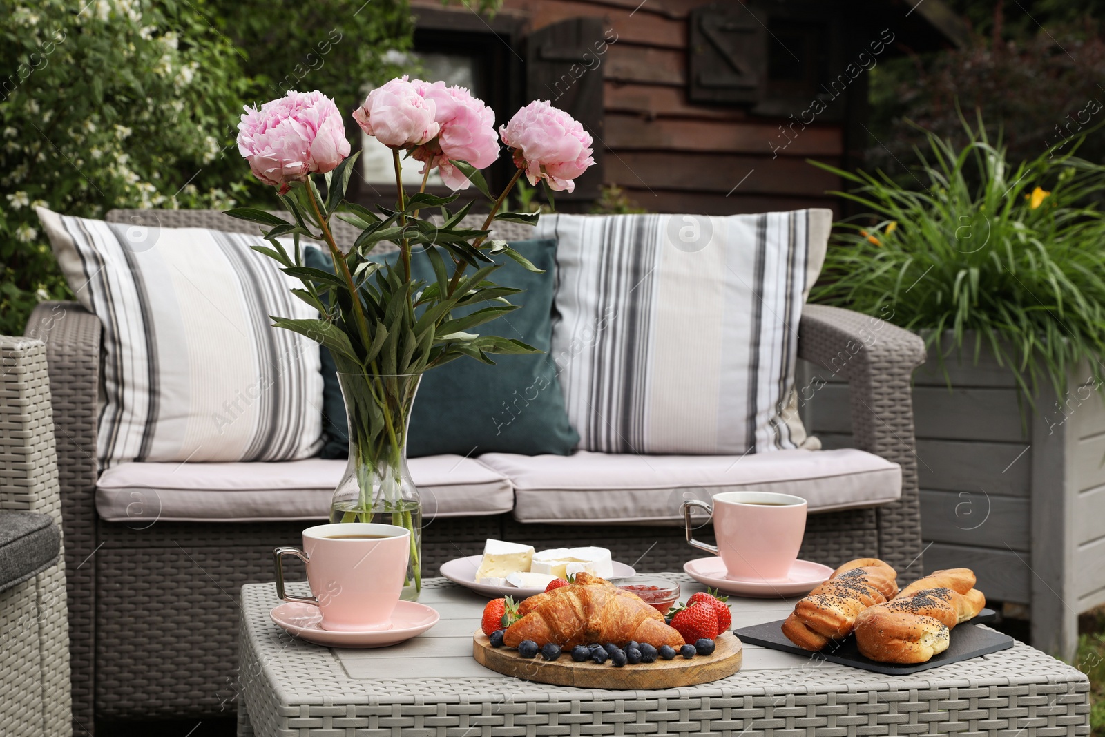 Photo of Morning drink, pastry, berries, cheese and vase with flowers on rattan table. Summer breakfast outdoors