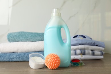 Photo of Orange dryer ball, detergents, clean towels and clothes on wooden table