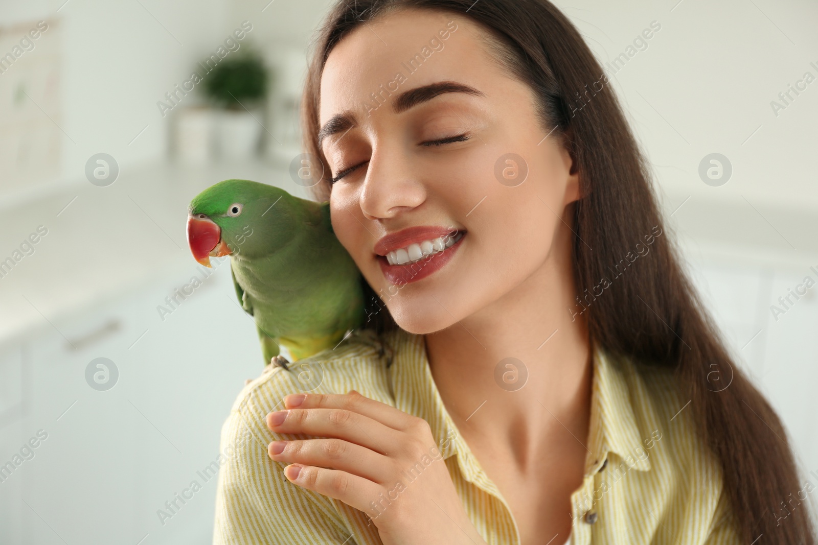 Photo of Young woman with Alexandrine parakeet indoors. Cute pet