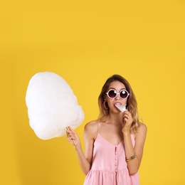 Photo of Happy young woman eating cotton candy on yellow background