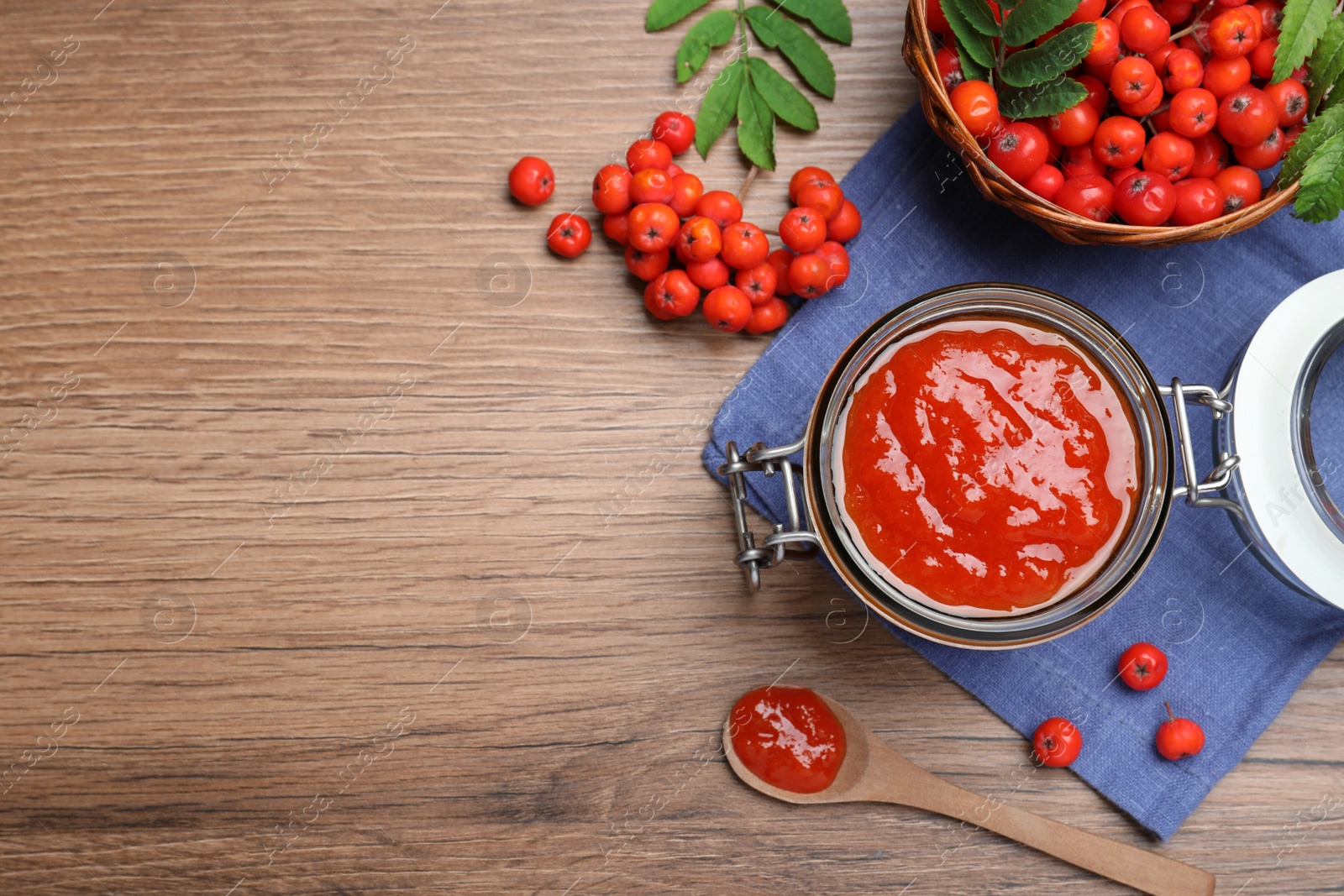 Photo of Flat lay composition with delicious rowan jam and berries on wooden table. Space for text