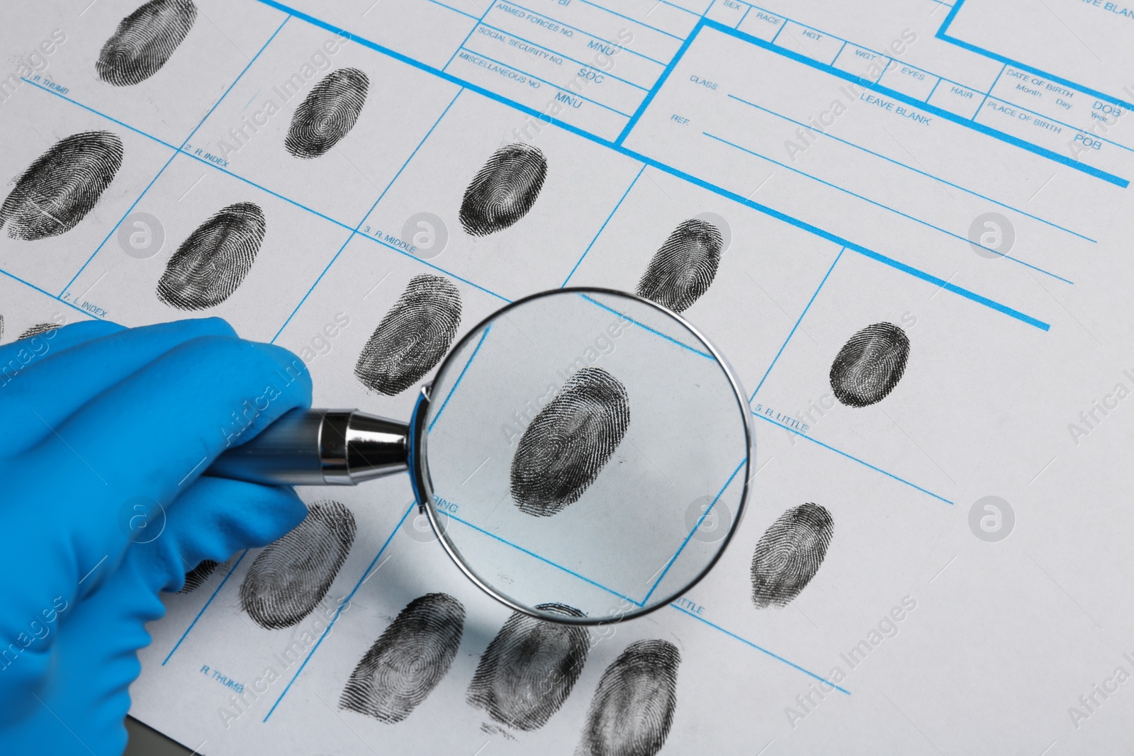 Photo of Criminalist studying fingerprints with magnifying glass, closeup