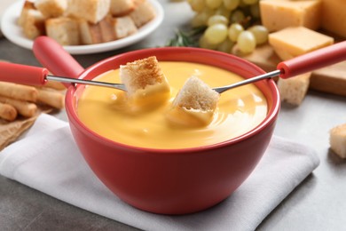 Pot of tasty cheese fondue and forks with bread pieces at grey table