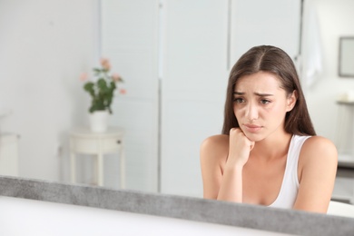 Photo of Young woman with eyelash loss problem looking in mirror indoors