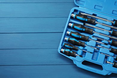 Set of screwdrivers in open toolbox on blue wooden table, top view. Space for text