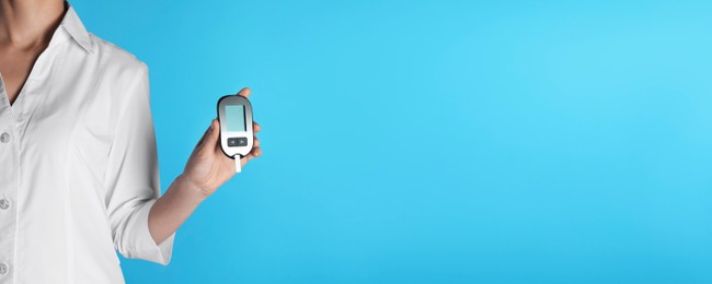 Image of Endocrinologist holding digital glucometer on light blue background, closeup. Banner design with space for text