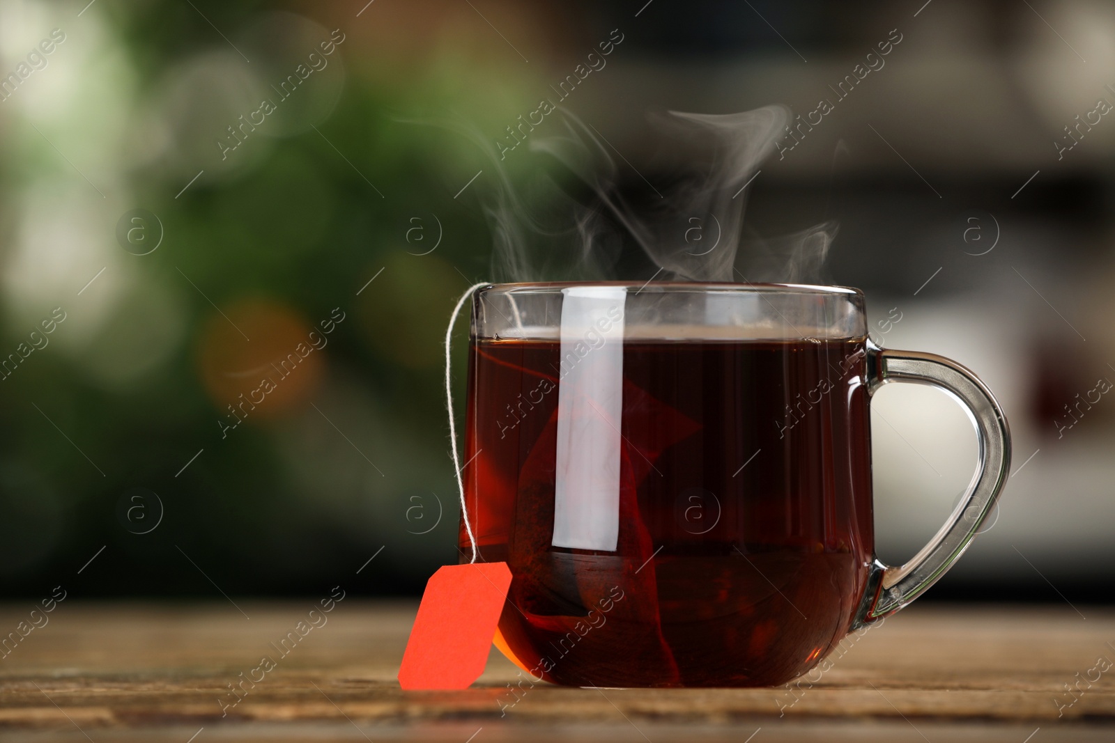 Photo of Tea bag in glass cup of hot water on wooden table against blurred background