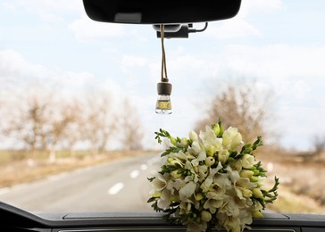 Image of Beautiful bouquet and air freshener hanging on rear view mirror in car