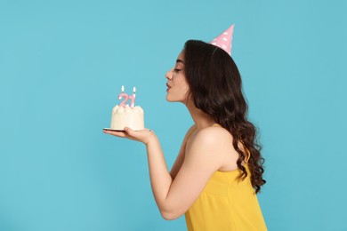Coming of age party - 21st birthday. Woman blowing number shaped candles on cake against light blue background