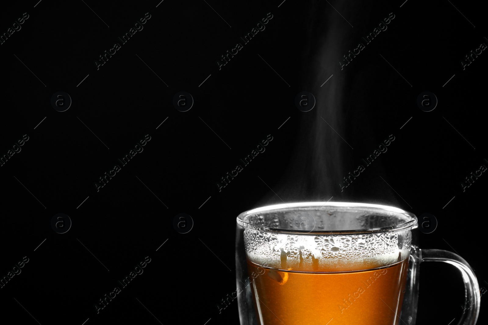 Photo of Glass cup of hot tea on black background, space for text