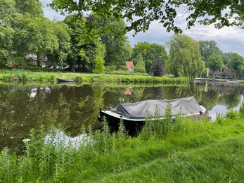 Photo of Beautiful view of city canal with moored boat surrounded by greenery