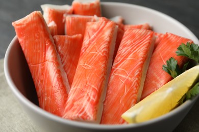 Photo of Crab sticks with lemon in bowl on grey background, closeup