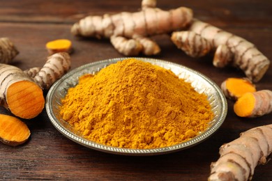 Photo of Plate with aromatic turmeric powder and cut roots on wooden table, closeup