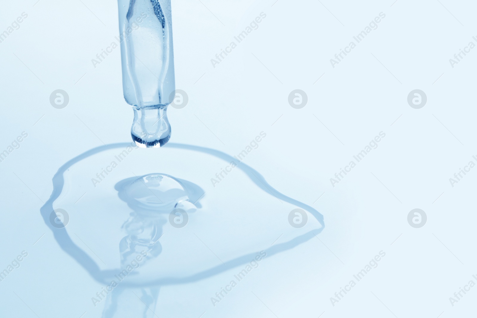 Photo of Dripping face serum from pipette on white background, closeup. Space for text