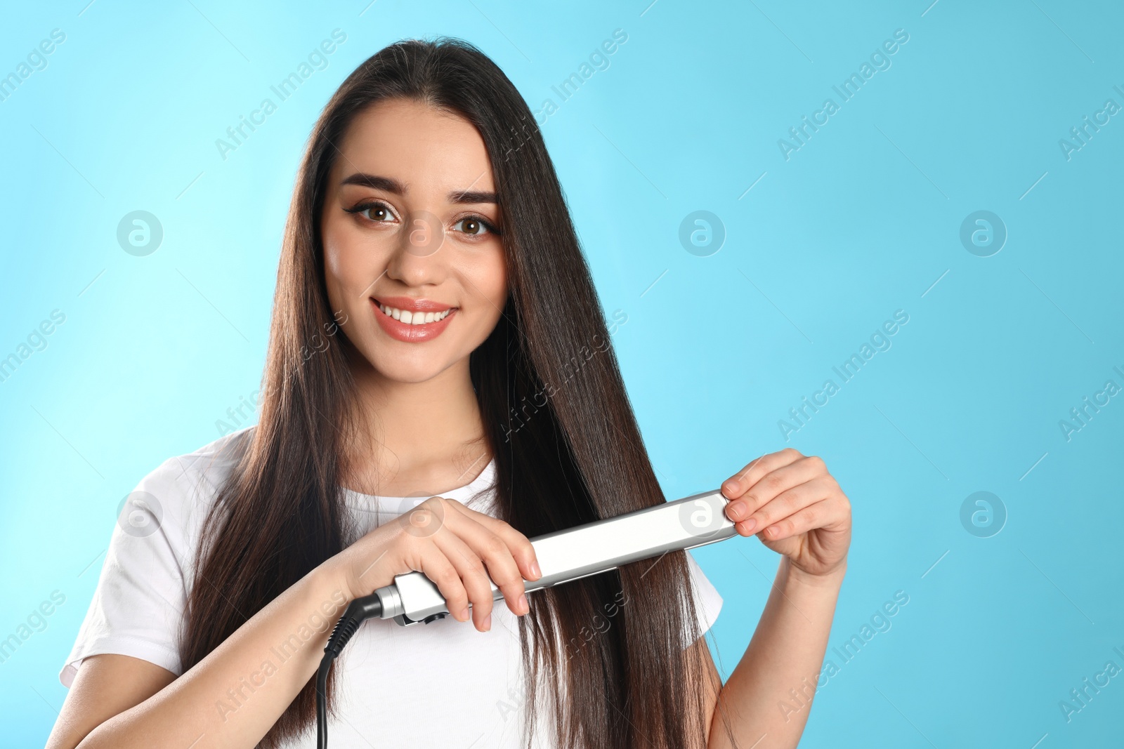 Photo of Happy woman using hair iron on color background. Space for text