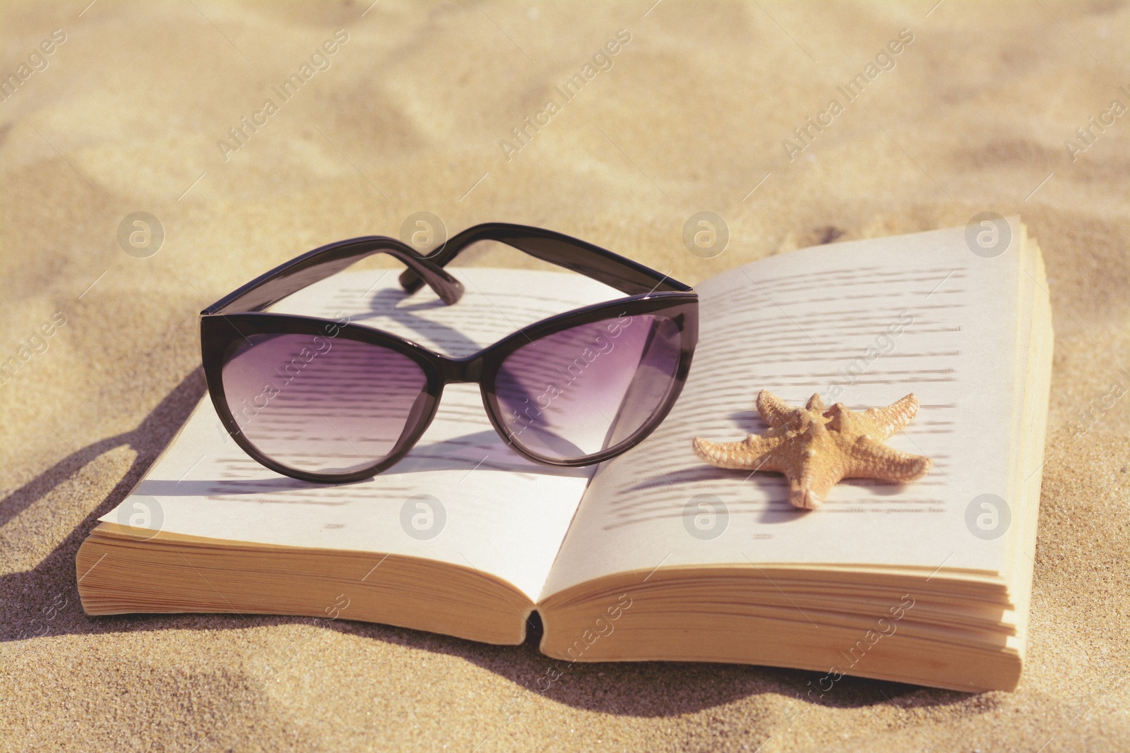 Photo of Beautiful sunglasses, book and starfish on sand, closeup