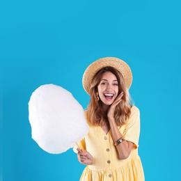 Emotional young woman with cotton candy on blue background