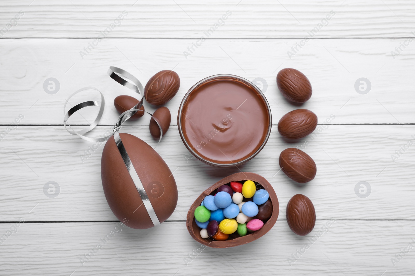 Photo of Delicious chocolate eggs, paste and candies on white wooden table, flat lay