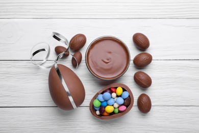 Delicious chocolate eggs, paste and candies on white wooden table, flat lay