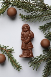 Photo of Flat lay composition with chocolate Santa Claus, fir tree twigs and sweets on white background