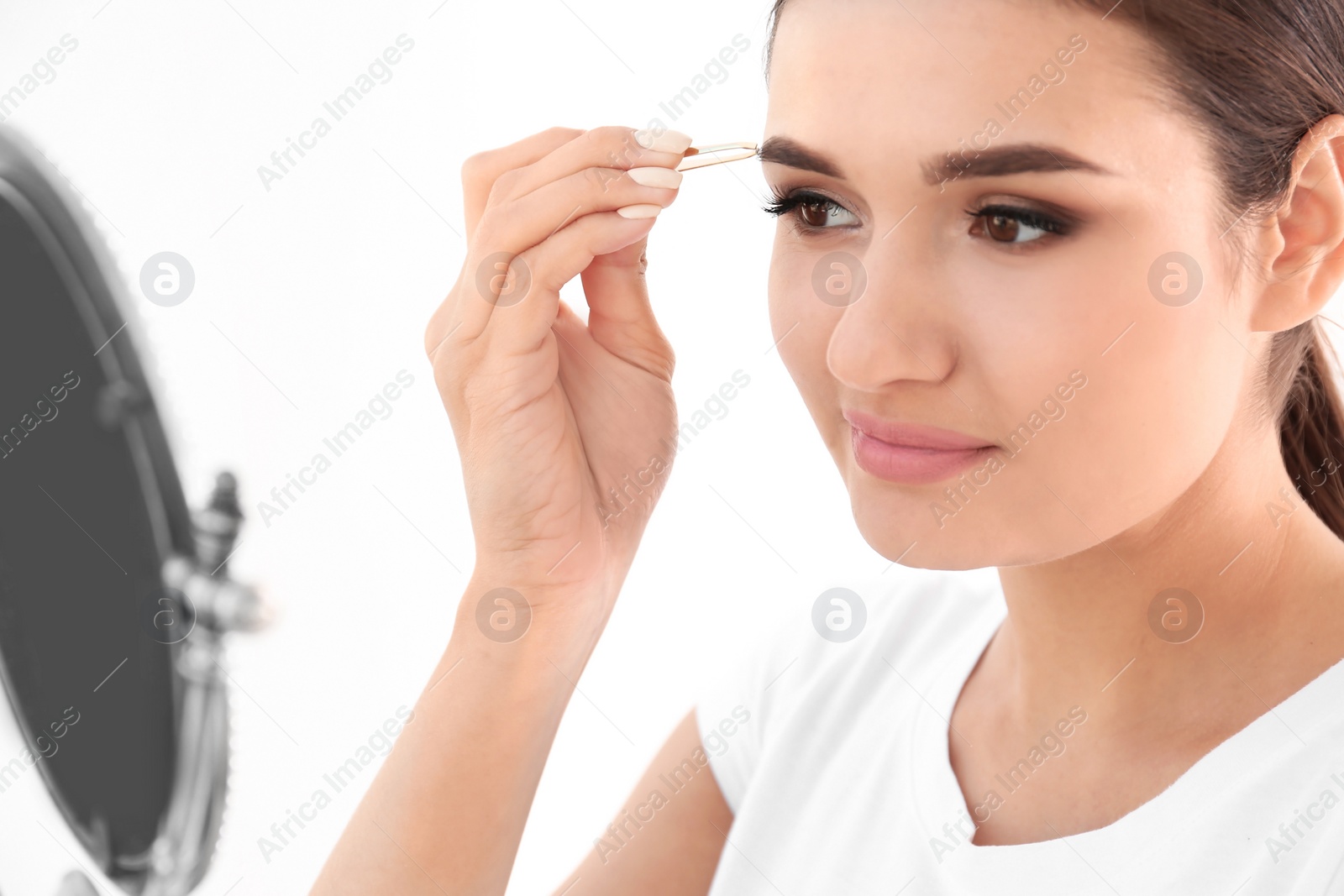 Photo of Young woman plucking eyebrow with tweezers, indoors