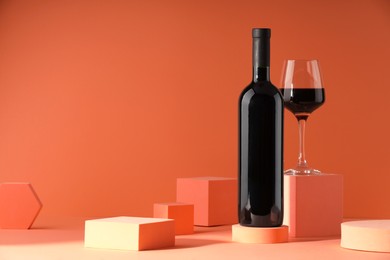 Stylish presentation of delicious red wine in bottle and glass on orange background. Space for text