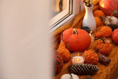 Photo of Composition with pumpkins and burning candles on window sill indoors