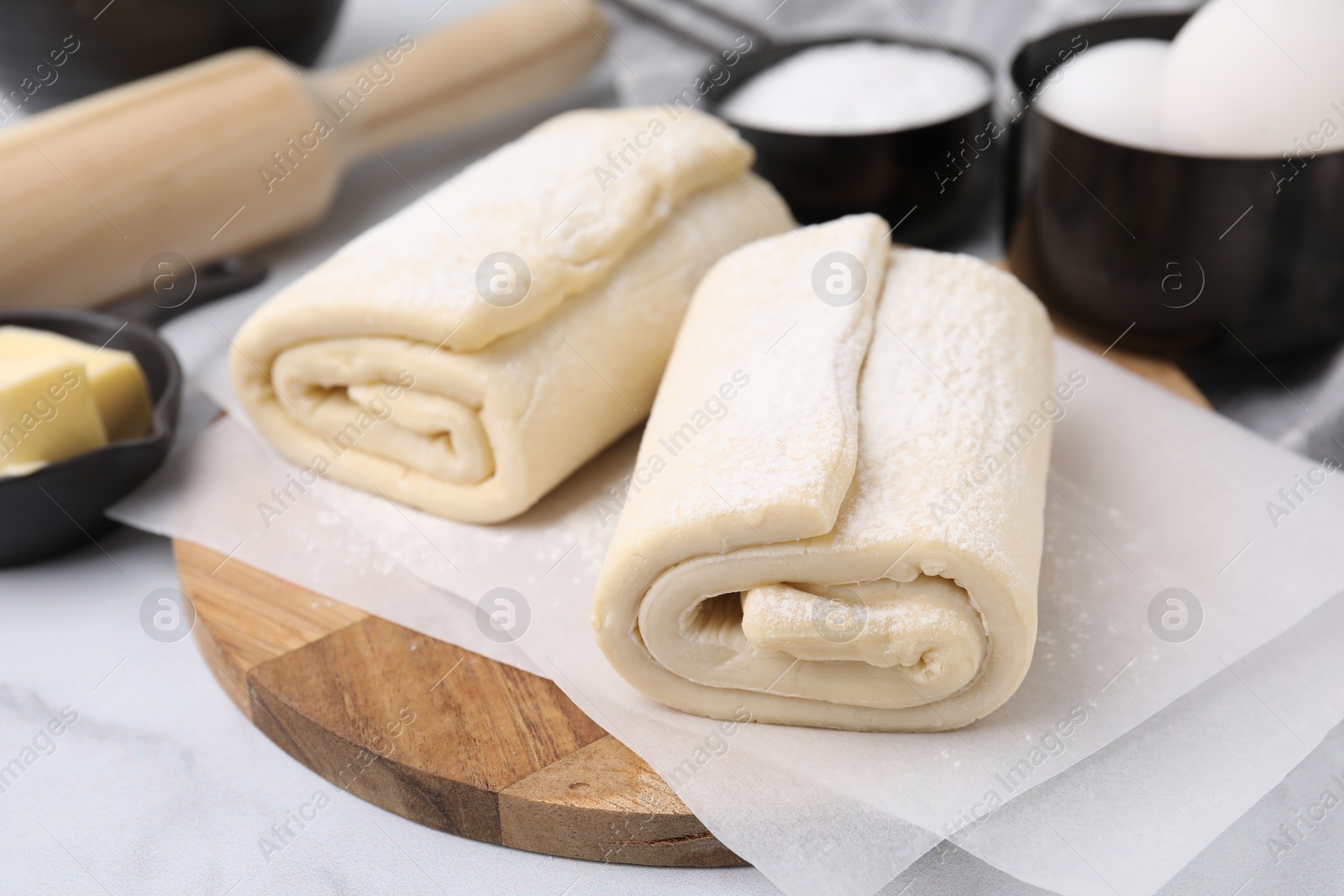 Photo of Raw puff pastry dough on white marble table, closeup