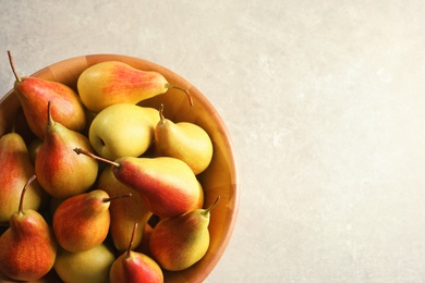 Photo of Bowl with ripe pears on light background, top view. Space for text