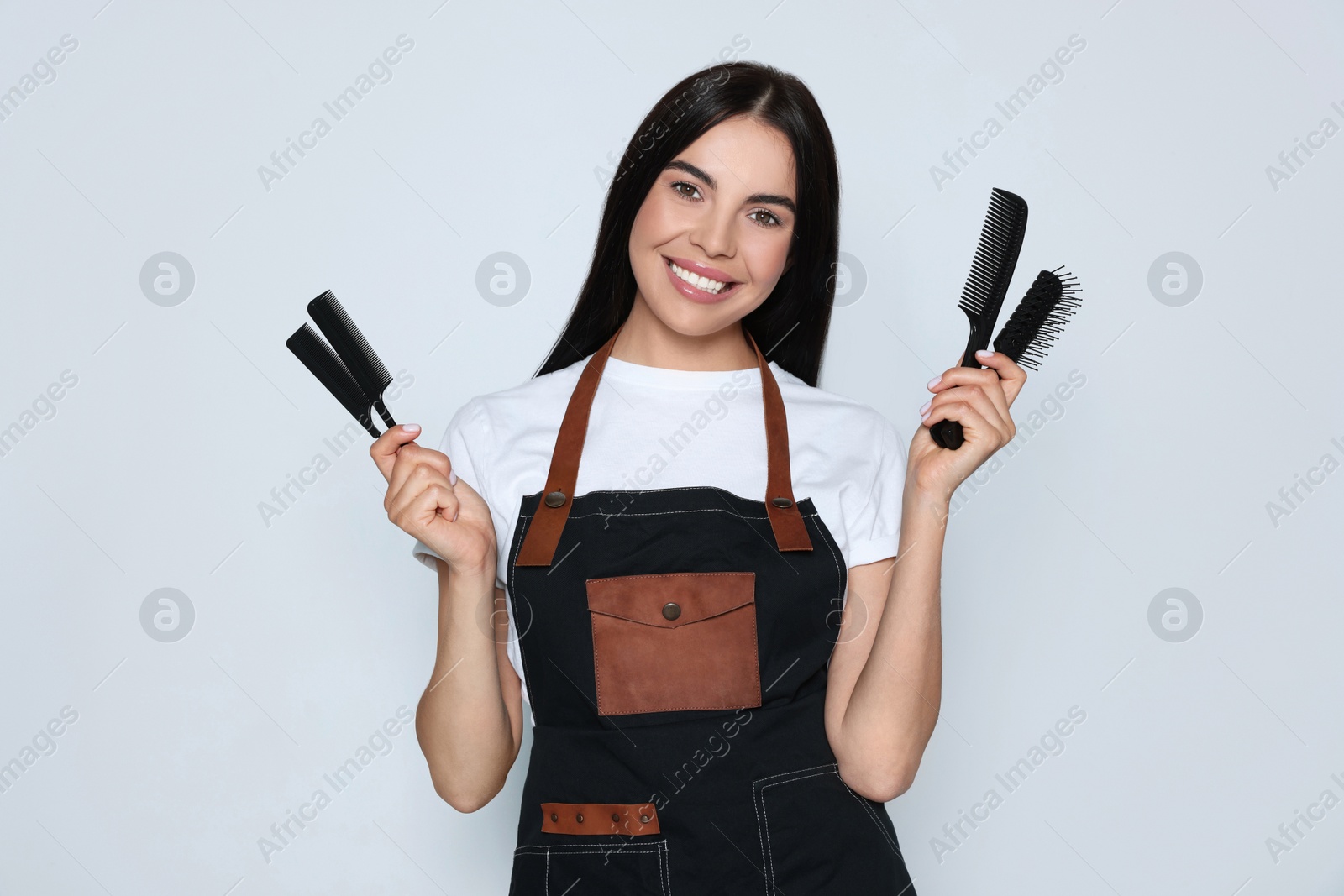 Photo of Portrait of happy hairdresser with professional combs on light background