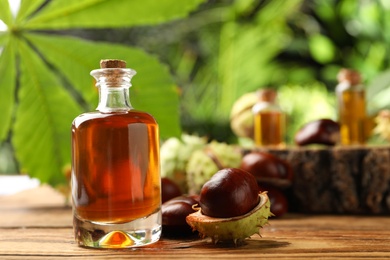 Photo of Chestnuts and bottle of essential oil on table against blurred background. Space for text