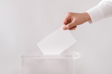 Woman putting her vote into ballot box on light grey background, closeup