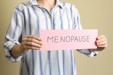 Photo of Woman holding card with word Menopause on beige background, closeup