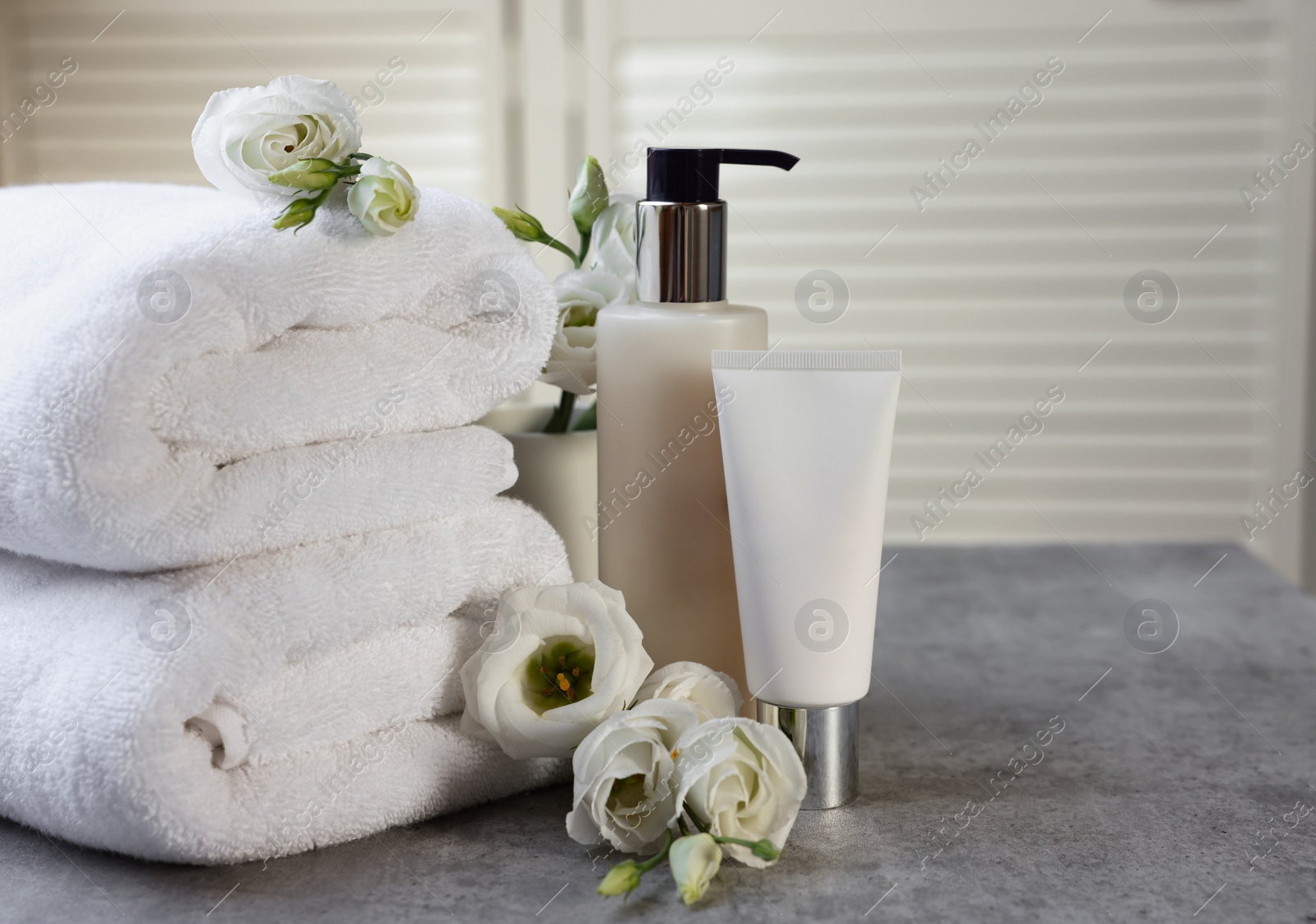 Photo of Cosmetic products, folded towels and flowers on gray marble table, space for text