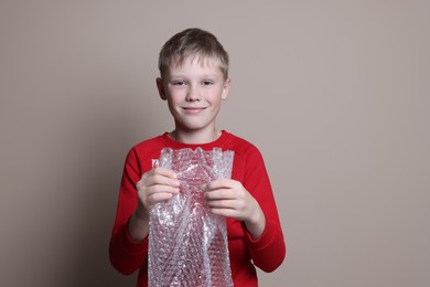 Photo of Boy popping bubble wrap on beige background. Stress relief