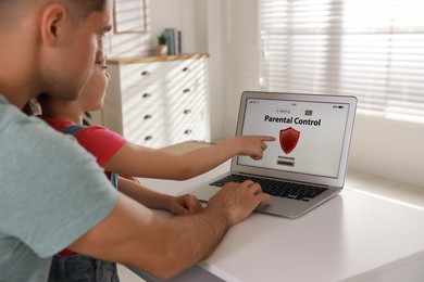 Photo of Father installing parental control app on laptop to ensure his child's safety at home