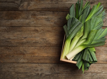 Photo of Crate of fresh raw leeks on wooden table, top view with space for text. Ripe onion