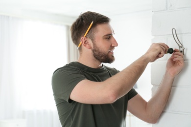 Photo of Young working man fixing clothes hook on wall at home, space for text