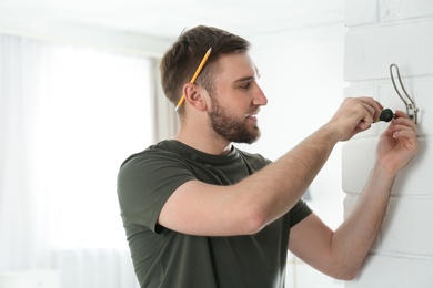 Young working man fixing clothes hook on wall at home, space for text