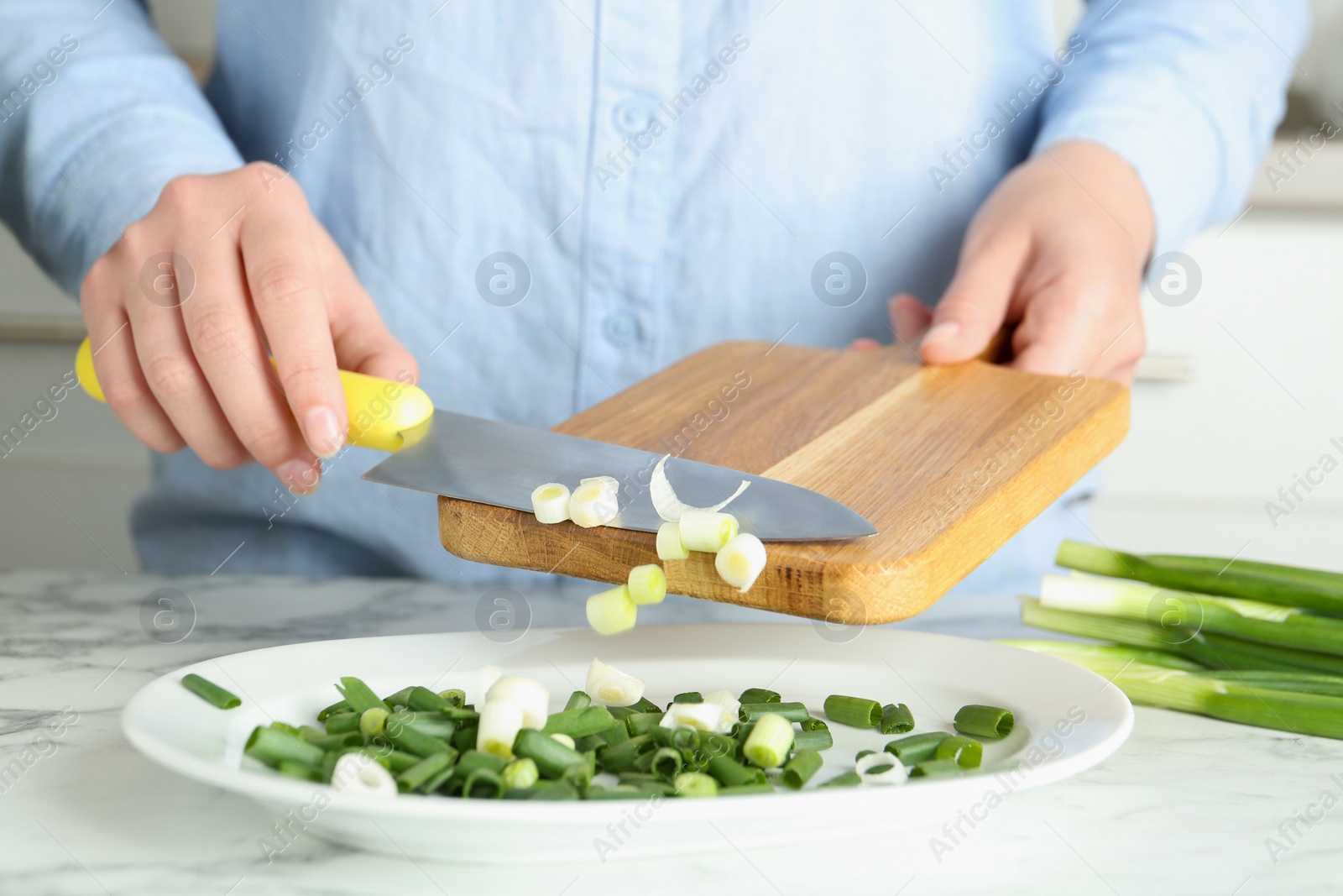 Photo of Woman putting chopped green spring onion into plate on white marble table, closeup