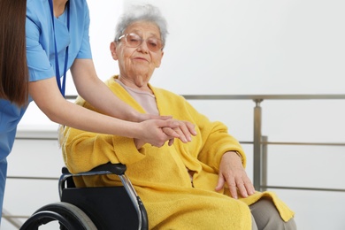 Photo of Nurse massaging hand of senior woman in wheelchair at hospital. Medical assisting