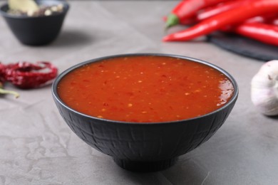 Spicy chili sauce in bowl on grey table