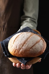 Photo of Woman holding freshly baked bread on black background, closeup